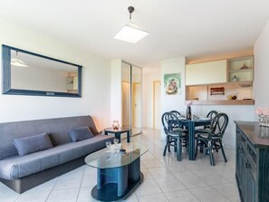 A modern living room with a grey sofa, a glass coffee table, and a dining area with a round table and chairs. - Grand Sud by Interhome (Canet-Plage)