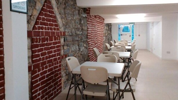 Un salón de conferencias con paredes de ladrillo y un arco de piedra, equipado con mesas y sillas plegables.