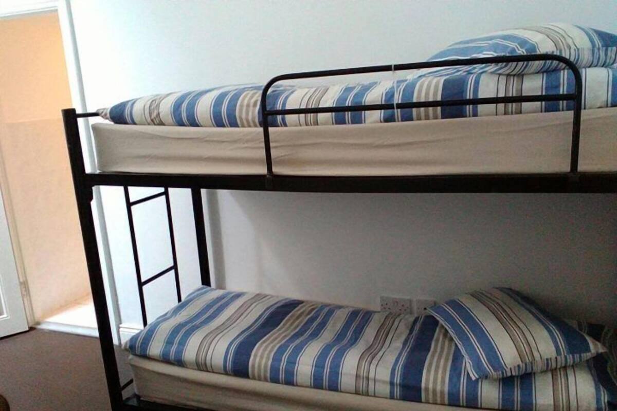 En køjeseng med stribet sengetøj i et rum med en glat væg og en dør.