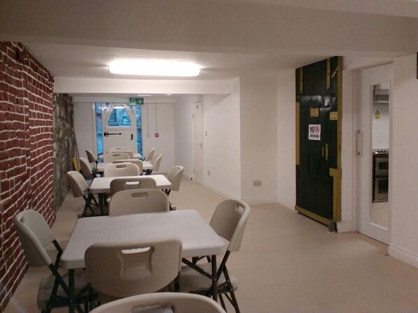 Zona de dinar amb taules i cadires blanques, una paret de maó i una porta amb un senyal de 'No Fumar'.