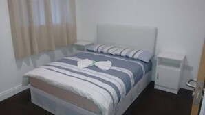 Una cama bien hecha con ropa de cama a rayas y una toalla doblada, una mesita de noche y una lámpara de noche en una habitación de hotel.