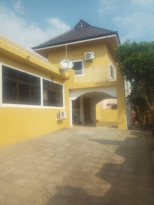 A two-story yellow building with a balcony, large windows, and an air conditioning unit. - Ama Serwaa Lodge (Taifa)