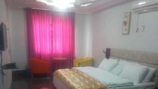 Una habitación de hotel con cama, escritorio, silla, ventana con cortinas y ventilador de techo.