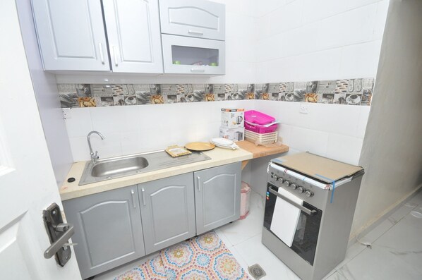 A compact kitchen with a sink, a stove, and grey cabinets. - B2 Self Catering Apartments (Serrekunda)