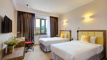 A hotel room with two beds, a desk, a chair, a TV, and a window with curtains.