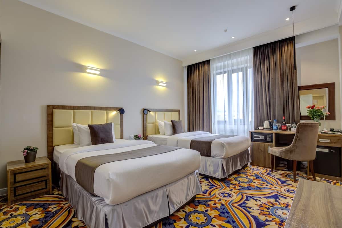 A hotel room with two beds, a desk, a chair, and a large window with curtains.