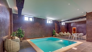 An indoor swimming pool with a tiled floor, surrounded by wicker seating and potted plants. - Garden Hotel & Spa (Bishkek)