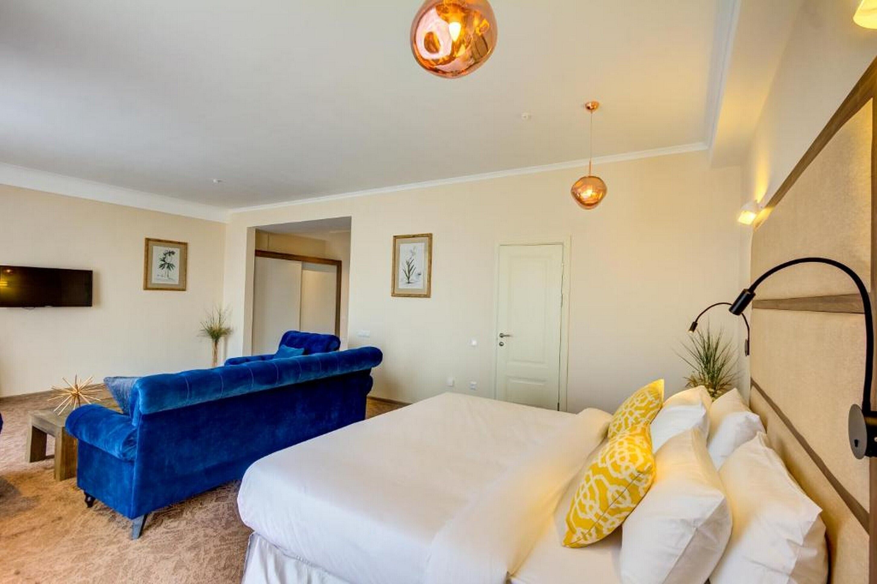 Ein modernes Schlafzimmer mit einem großen Bett, einem blauen Sofa und einem flachbildfernseher an der Wand.