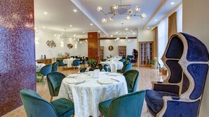 A dining area with round tables, green upholstered chairs, and a decorative wall. - Garden Hotel & Spa (Bishkek)