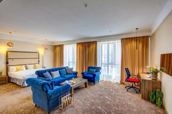 A hotel room with a large bed, two blue sofas, a coffee table, a desk, and a cactus plant. - Garden Hotel & Spa (Bishkek)