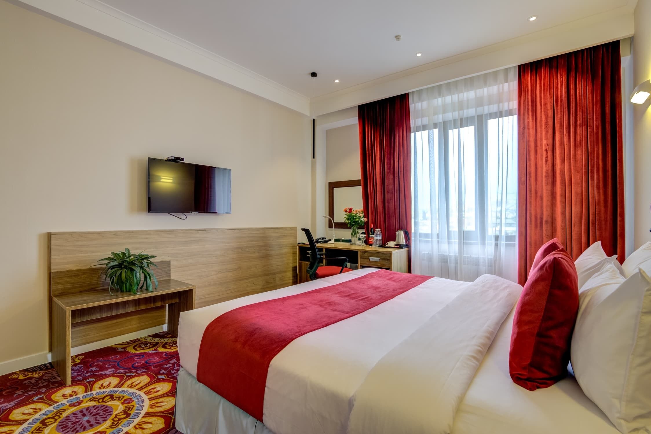 Una habitación de hotel con cama, escritorio, silla, televisión y ventana con cortinas.