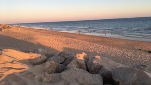 Ein Strand mit großen Felsen im Vordergrund und Menschen, die am Ufer entlanggehen.