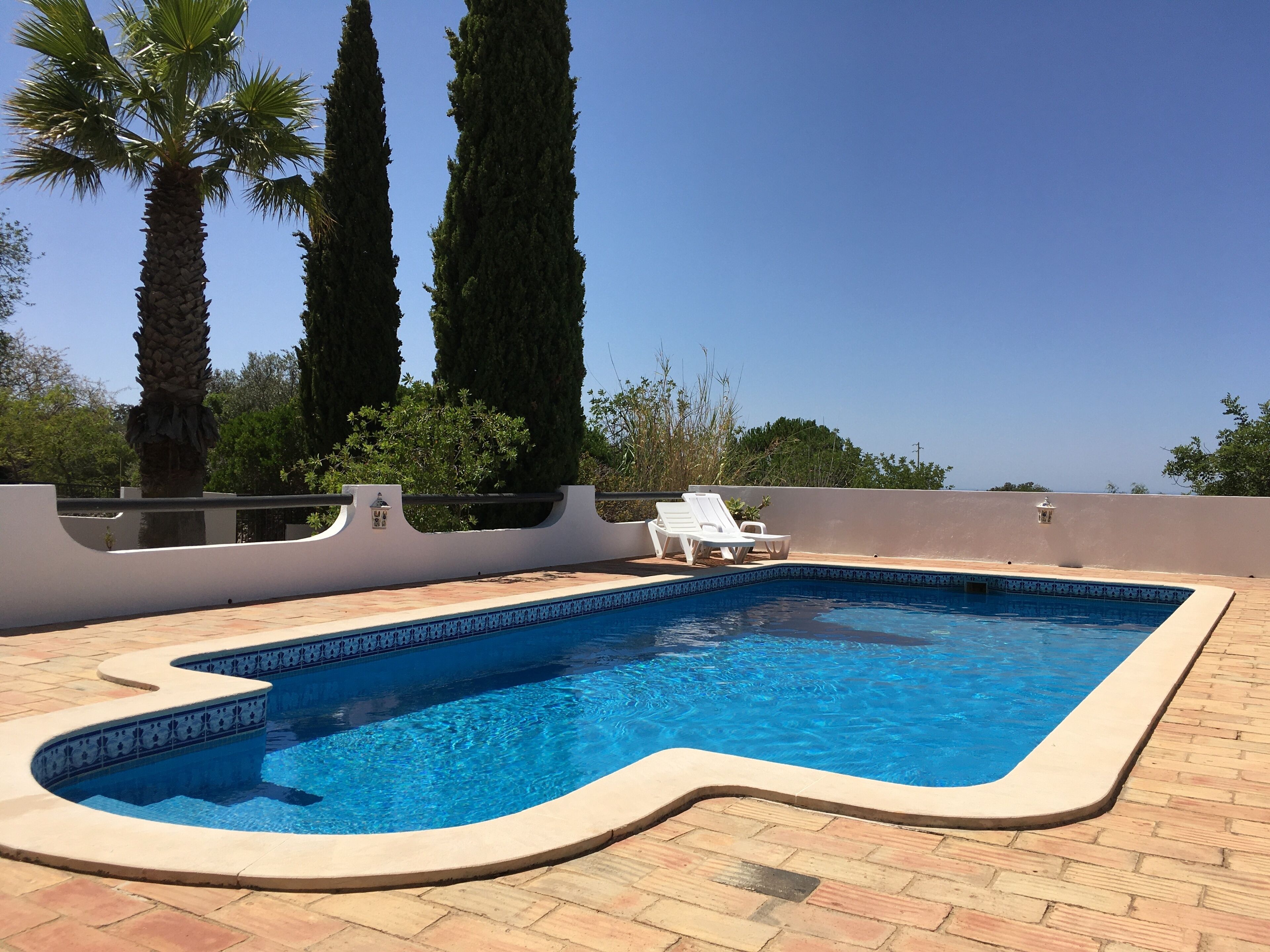 A swimming pool with a tiled edge, surrounded by a brick patio.