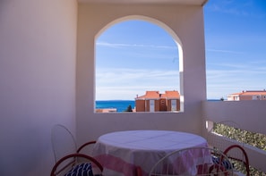 A balcony with a table and chairs, a view of the sea, and a building with red roofs. - Apartments Antonia (Novalja)