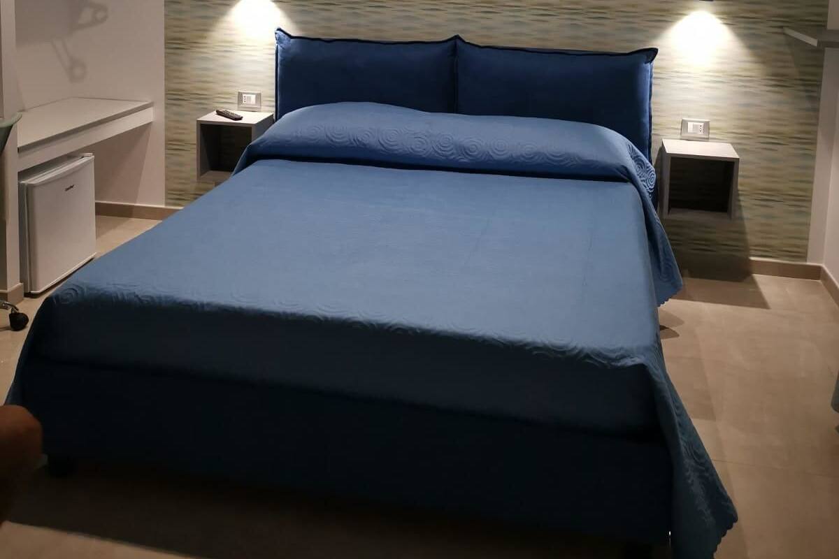 A bedroom with a large bed, two bedside tables, a small desk, and a wall-mounted shelf.