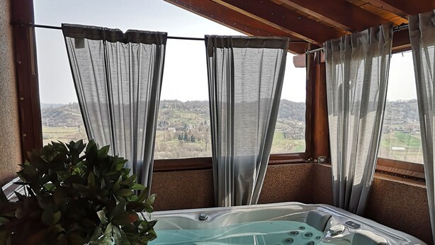 A hot tub with a wooden bench and a potted plant, a wooden table, and a view of a landscape through sheer curtains. - Viksa with Hot Tub (Zagreb)