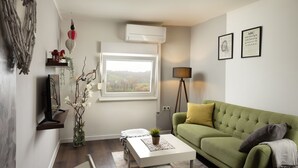 A living room with a green sofa, white coffee table, and a window with a view of a cityscape. - Viksa with Hot Tub (Zagreb)