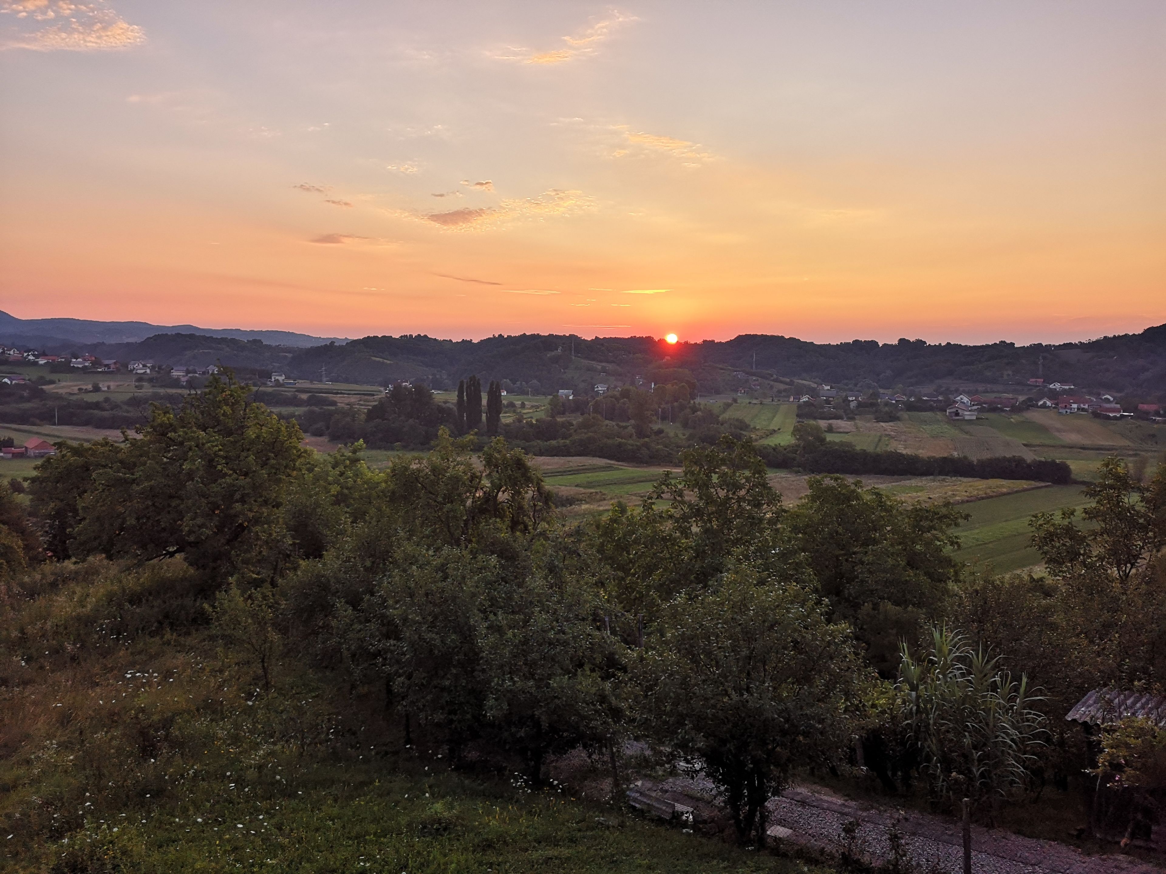 A rural landscape with a sunset, hills, and scattered houses.