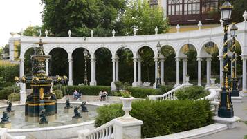 A classical garden with a fountain, white columns, and ornate lamp posts.