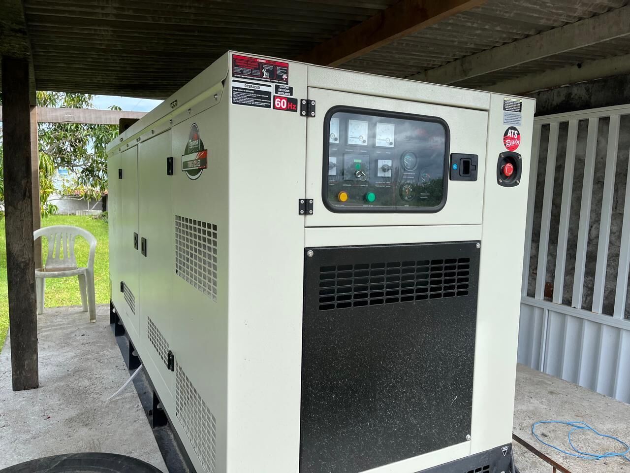A portable generator with a control panel, placed outdoors under a shelter.