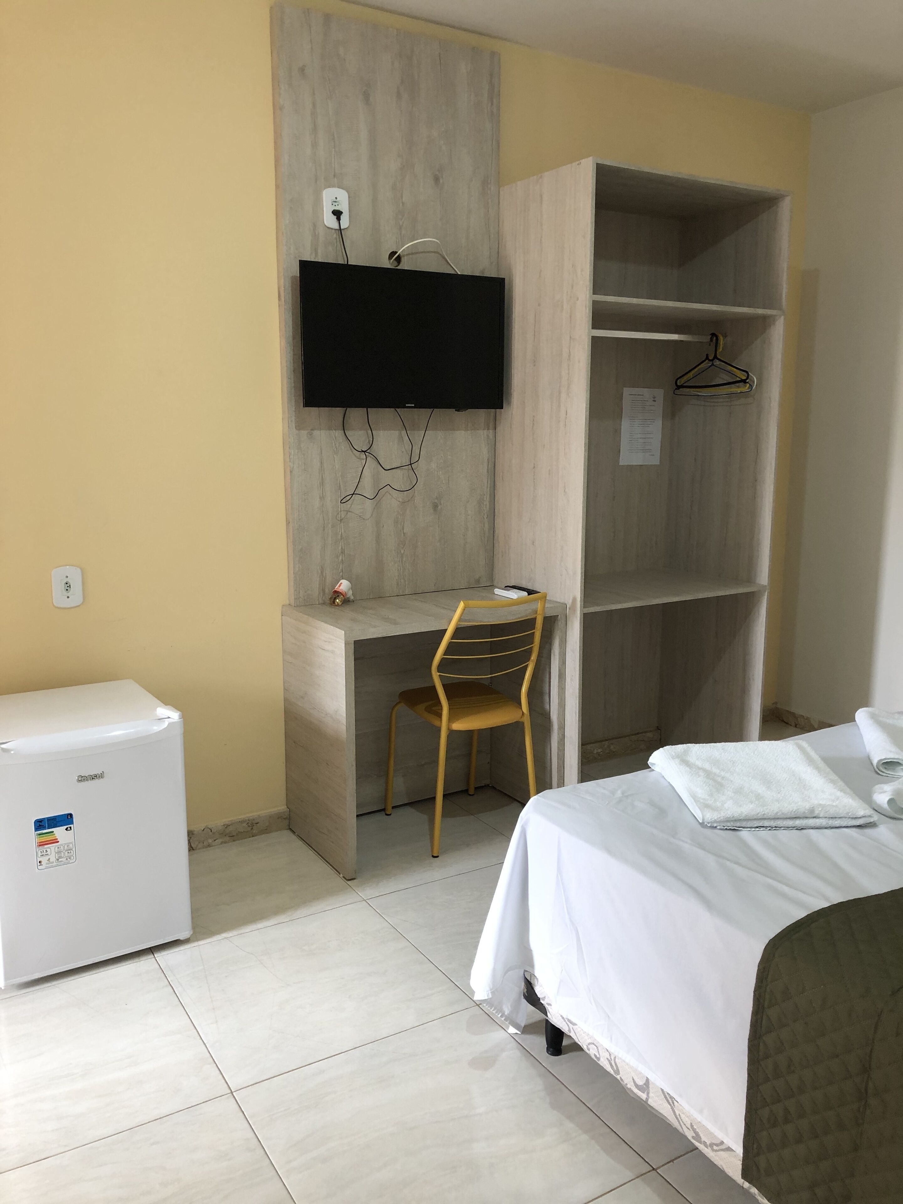 Camera d'albergo con un letto, una scrivania con una sedia, una televisione a parete e un piccolo frigorifero.