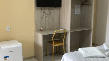 Een hotelkamer met een bed, een bureau met stoel, een aan de muur bevestigde televisie en een kleine koelkast.