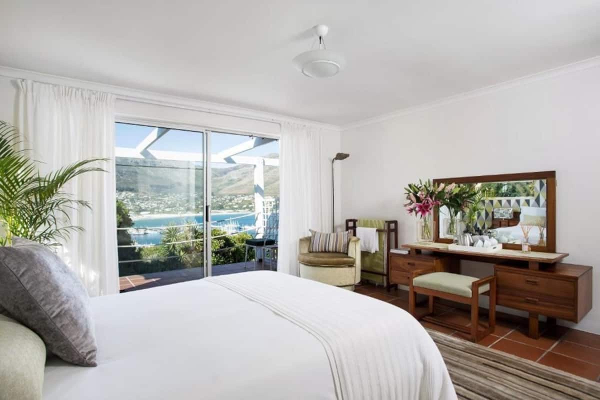 Un dormitorio con una cama grande, un escritorio, una silla y vistas a un paisaje costero a través de una puerta corredera.