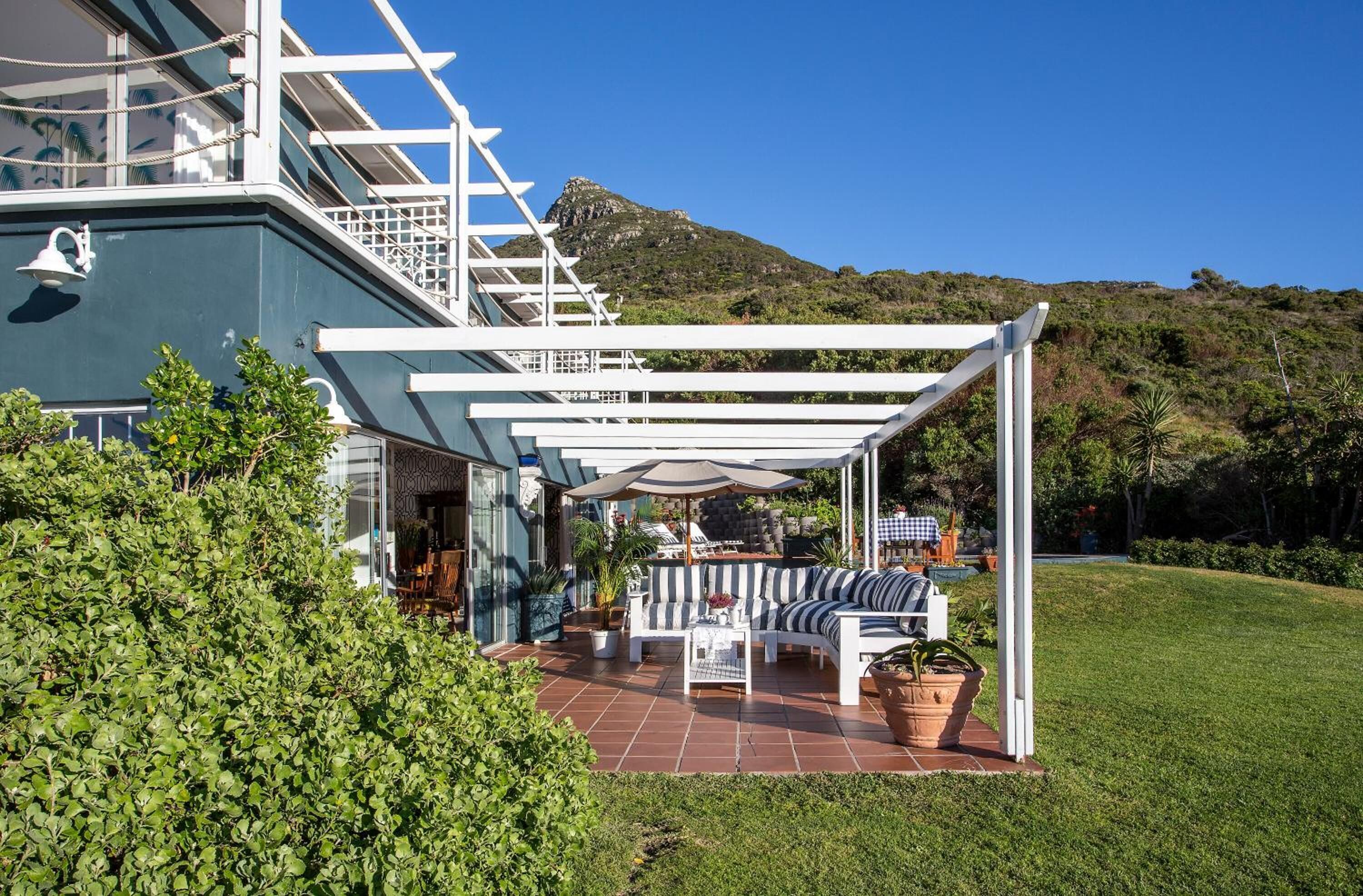 Een overdekt terras met een witte pergola, een zithoek met een gestreepte bank en uitzicht op een berg.