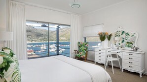 A hotel room with a large bed, a desk, and a view of a harbor with boats. - Poseidon Guest House (Cape Town)