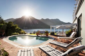 A swimming pool with lounge chairs, a table, and a view of mountains and the sea. - Poseidon Guest House (Cape Town)