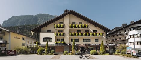 Een hotel met balkons vol planten, een fiets ervoor en een berg op de achtergrond.