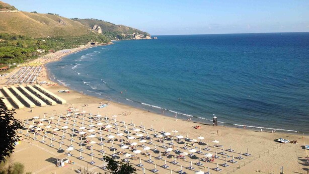 A beach with rows of sunbeds and umbrellas, a clear sky, and a calm sea. - Casa Ares Sperlongaresort (Sperlonga)