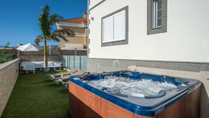 Ein Whirlpool in einem Hinterhof mit Steinmauer, einer Palme und einem weiß gestrichenen Gebäude mit Fensterläden.