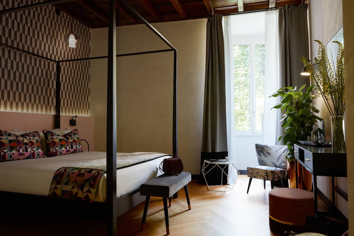 A bedroom with a four-poster bed, a bench, a small table, a chair, and a potted plant.