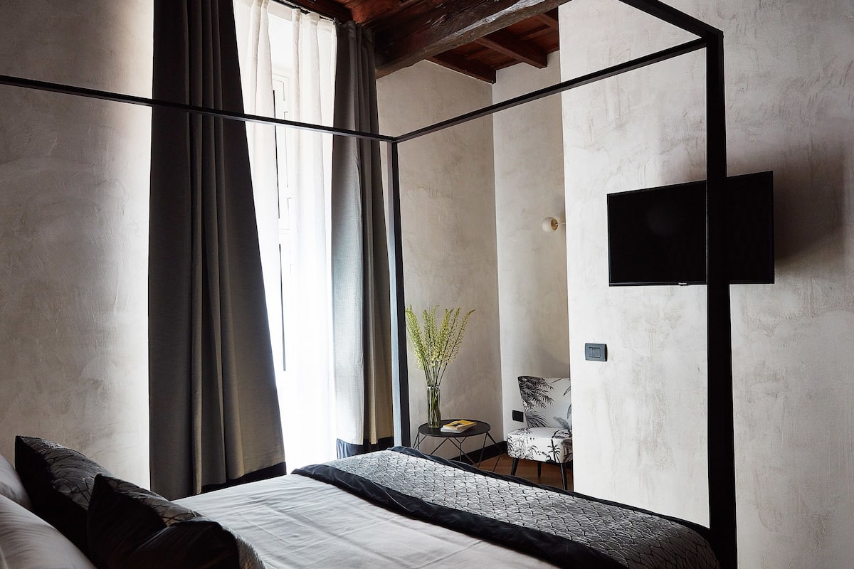 A modern bedroom with a large bed, a flat-screen TV mounted on the wall, and a small table with a vase of flowers.