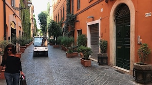 A cobblestone street lined with orange buildings, a parked car, and potted plants. - Naman Hotellerie Via Margutta (Rome)