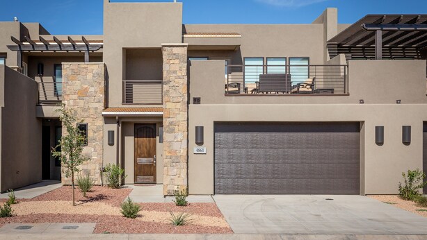 Une maison moderne à deux étages, dotée d’une façade en pierre, d’un grand garage et d’une petite terrasse avec coin salon extérieur.