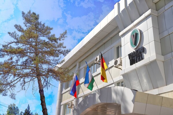 A building with a modern architectural design, featuring a prominent logo and multiple flags displayed outside. - VIARDO Hotel (Tashkent)