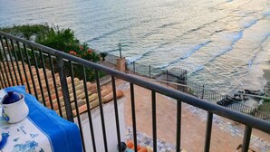 A balcony with a view of the sea, a tiled floor, and a table with a blue cloth and a ceramic pot.