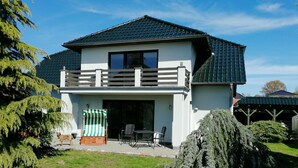 A two-story house with a balcony, a patio with outdoor furniture, and a well-maintained garden. - Appartements Süssling (Glowe)