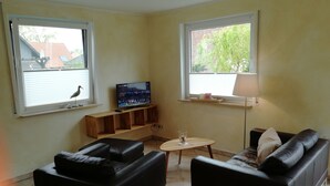 A living room with two black sofas, a wooden coffee table, a TV on a wooden stand, and a lamp on a table. - Appartements Süssling (Glowe)