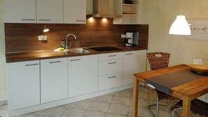A compact kitchen with white cabinets, a wooden countertop, a built-in coffee maker, and a hanging light fixture. - Appartements Süssling (Glowe)