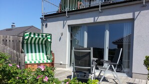 A patio with a green and white striped beach chair, a metal chair, and a glass door leading to a balcony. - Haus Alt Glowe (Glowe)