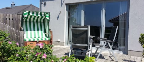 Eine Terrasse mit einem Liegestuhl in Grün und Weiß gestreift, einem Metallstuhl und einer Glastür, die zu einem Balkon führt.