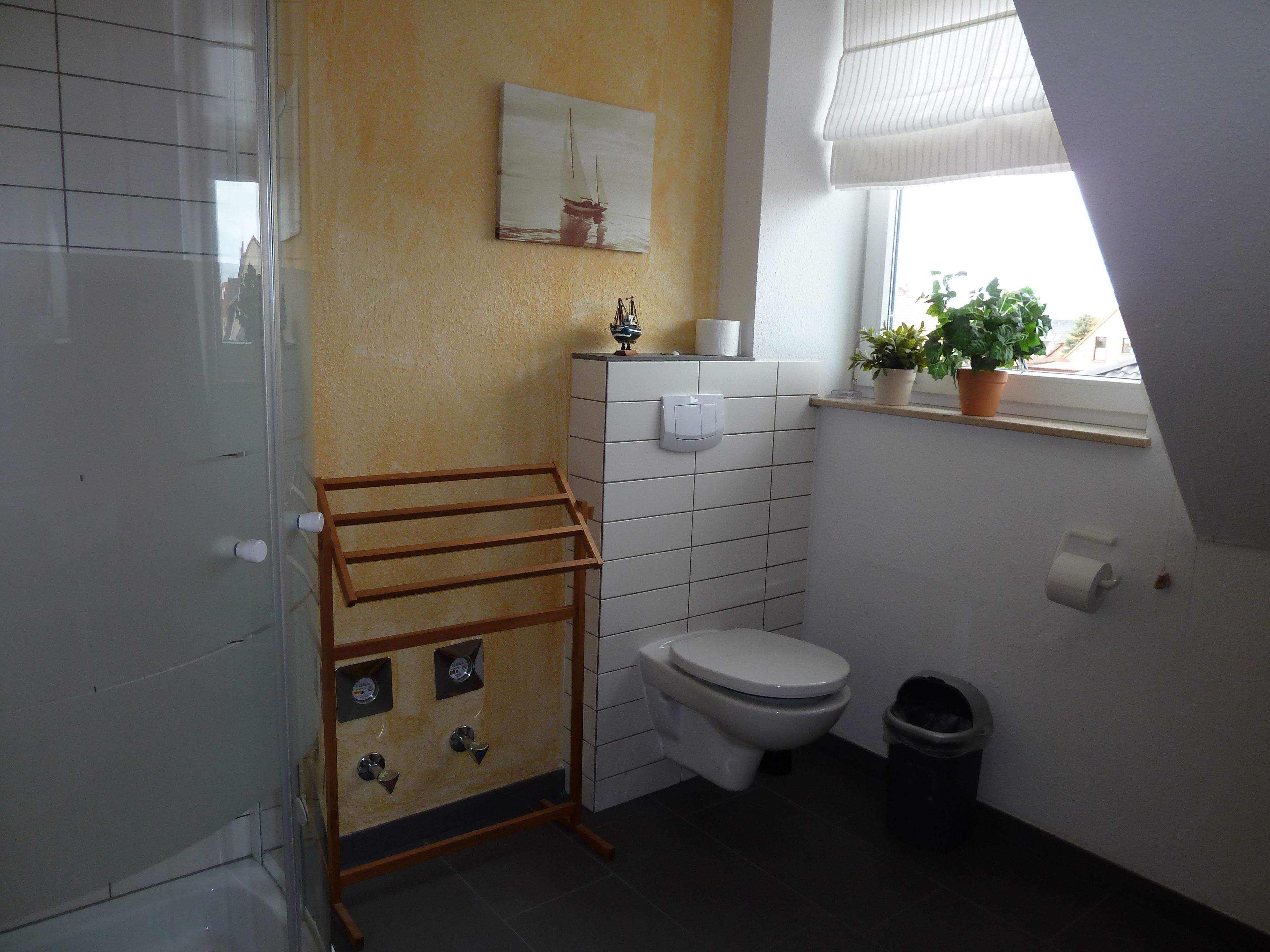 Un baño con inodoro, lavamanos, toallero y ventana con planta.