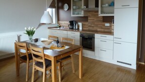 A modern kitchen with wooden cabinets, a built-in oven, and a dining area with a wooden table and chairs. - Haus Alt Glowe (Glowe)