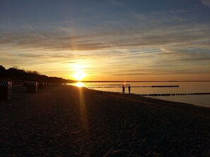 Une plage avec un coucher de soleil, une eau calme et une jetée.