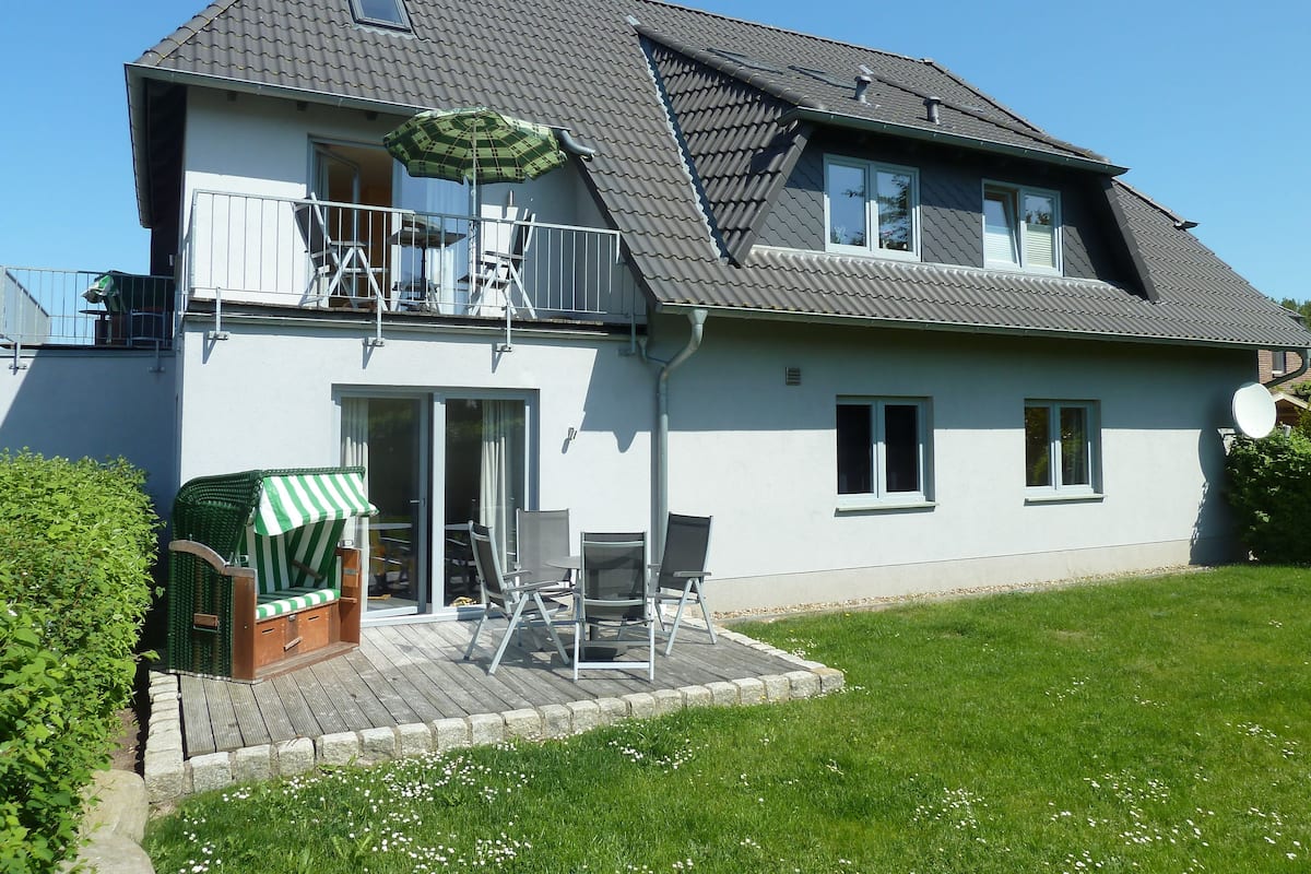 Une maison à deux étages avec un balcon, une terrasse dotée de mobilier d’extérieur et un jardin.