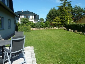 Une pelouse bien entretenue, agrémentée d’une table et de chaises de patio, entourée d’une bordure en pierre et d’une variété d’arbustes et d’arbres.