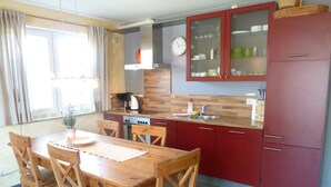 A compact kitchen with wooden cabinets, a built-in oven, and a dining area with a wooden table and chairs. - Haus Alt Glowe (Glowe)